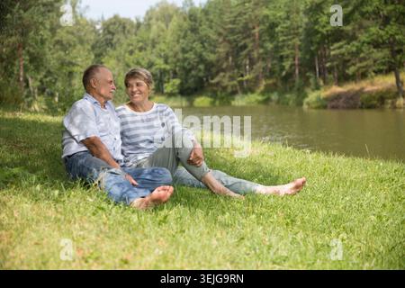 Felice coppia anziana seduta d'estate vicino al lago Foto Stock