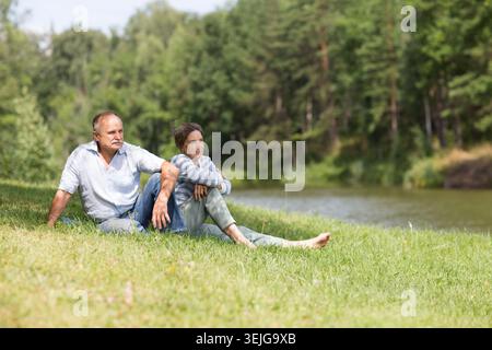 Felice coppia anziana seduta d'estate vicino al lago Foto Stock