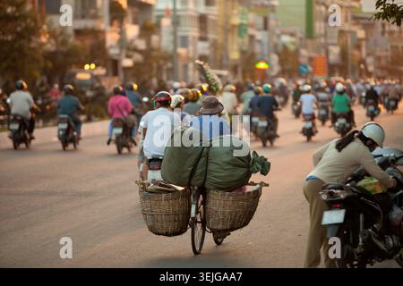 Ora di punta serale con motociclisti nella città asiatica, con due cestini per la bicicletta. Foto Stock