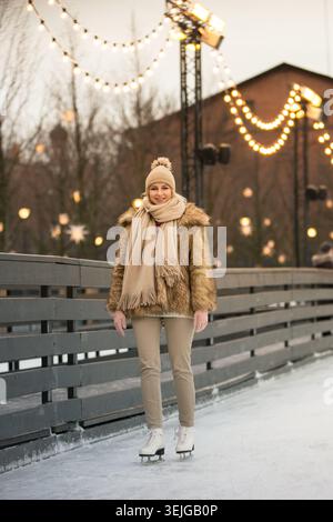 Giovane donna in pelliccia, cappello beige con pompon, sciarpa pattinaggio su ghiaccio, all'aperto in inverno Foto Stock