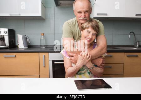 Felice e sorridente coppia anziana innamorata che abbraccia in cucina. Foto Stock