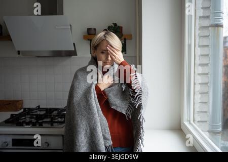 Donna di mezza età con espressione dolorosa che soffre di mal di testa e alta temperatura causata dall'influenza Foto Stock