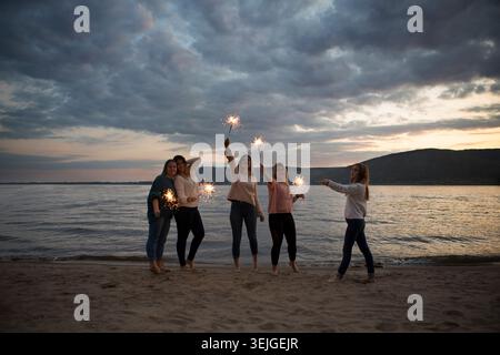Gruppi di amici felici che si divertono con scintillanti che fanno festa sulla spiaggia. Foto Stock