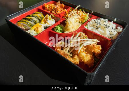 Pranzo giapponese al Bento Box con squilli di merluzzo fritti, sushi Rolls, insalata, riso, zenzero e wasabi sottaceto, involtini di pesce Maki, pesce giapponese, specialità di pesce asiatiche Foto Stock