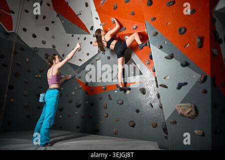 Due donne condividono la pratica del bouldering nella moderna palestra di arrampicata. Foto per supporto, partnership formativa, fiducia, cultura dello sport, pubblicità benessere, promozione Foto Stock
