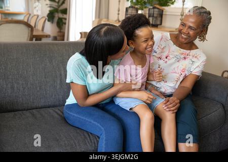 Famiglie diverse sedute a stretto contatto sul divano grigio scuro in un luminoso soggiorno con piante in vaso. Famiglia, multigenerazionale, insieme Foto Stock