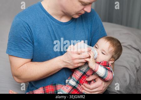 Adorabile bambino che beve latte dal biberon in mano al padre Foto Stock
