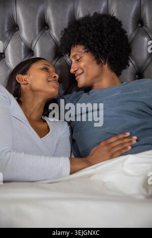 Diverse coppie che si trovano fianco a fianco sul letto con piumone bianco su testiera tufted grigio scuro. Romantico, intimo, relax, co Foto Stock