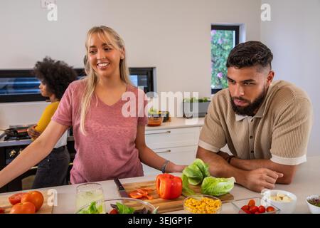Diversi amici affettano peperoni sul tagliere nella cucina di casa, spazio per copiare. Cucina, collaborazione, rustica, freschezza, s Foto Stock