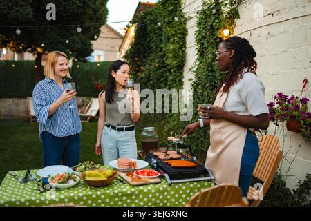 Diverse donne e amiche che si divertono insieme con un barbecue nel cortile Foto Stock