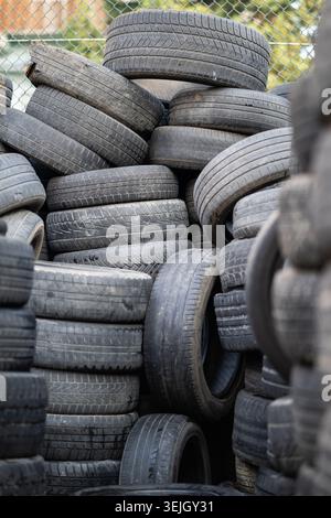 Vecchi pneumatici di gomma usati impilati con pali alti. Rifiuti pericolosi che richiedono il riciclaggio e lo smaltimento. Foto Stock