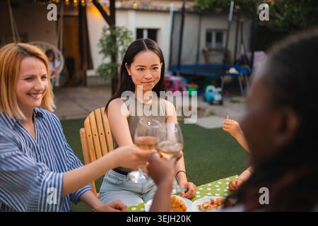 Diversi giovani adulti che si godono un brindisi con vino nel giardino sul retro Foto Stock
