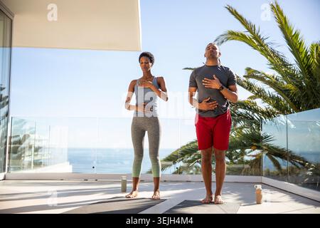 Diversi partner di allenamento che praticano la respirazione sui tappetini da yoga con bottiglie d'acqua sulla terrazza sull'oceano. Fitness, benessere, serenità, rel Foto Stock