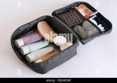 Kit cosmetico da viaggio nero sul letto. flaconi cosmetici colorati confezionati in sacchetto di plastica, pillole e articoli igienici per i viaggi Foto Stock