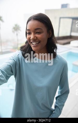 Donna afroamericana in piedi sul tetto che si avvicina in avanti accanto alla piscina vicino a ringhiere di vetro e palma. Città, tempo libero, relax, Foto Stock