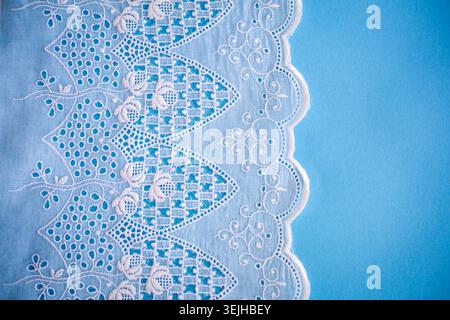 Motivo in pizzo, dettaglio di una tovaglia isolata su sfondo blu. Confine artistico. Artigianato, vintage. Concetto di hobby. Vista dall'alto. Foto Stock