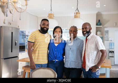 Famiglia diversificata in una cucina moderna intorno al piano di appoggio dell'isola con sgabelli e lampade a sospensione. Famiglia, moderno, interni, stile di vita, collaborazione, Foto Stock