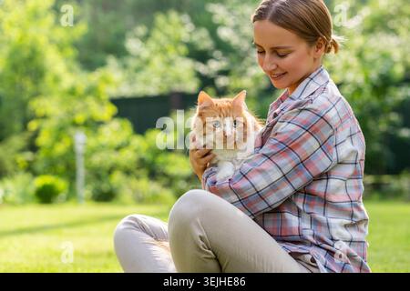 Primo piano di una donna sorridente in camicia a quadri che abbraccia e abbraccia con tenerezza e amore gatto domestico dello zenzero, accarezzando la h Foto Stock