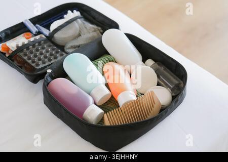 Kit cosmetico da viaggio nero sul letto. bottiglie cosmetiche colorate, pillole e articoli igienici da viaggio Foto Stock