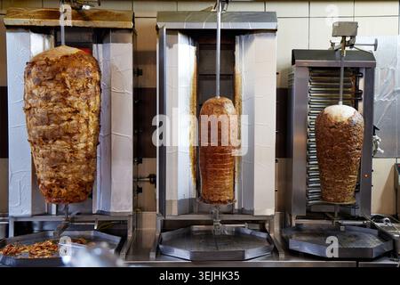 Tre grandi coni di carne di kebab doner che ruotano su griglie di girarrosto verticali in una cucina di un ristorante fast food. Foto Stock