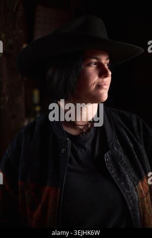 Cowgirl in un ampio cappello guarda in lontananza in un ranch poco illuminato Foto Stock