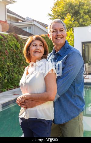 Le coppie senior si affacciano sulla piscina nel cortile periferico che si affaccia sulla siepe e sulla piscina. Romantico, all'aperto, tempo libero, tran Foto Stock