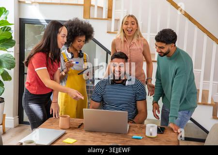 Diversi colleghi che collaborano intorno a un tavolo in legno in un ufficio domestico utilizzando un computer portatile e un tablet. Collaborazione, lavoro di squadra, moderno, kre Foto Stock