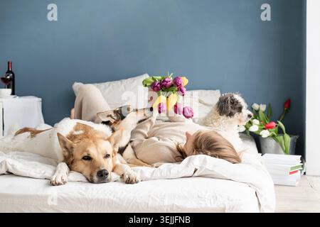 Giovane donna felice sdraiata nel letto con i suoi cani Foto Stock