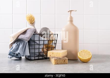 Prodotti per la pulizia ecologici in cestello in filo metallico con panni riutilizzabili, spugne e biberon ricaricabile sul piano di lavoro della cucina. Pulizia della casa sostenibile Foto Stock