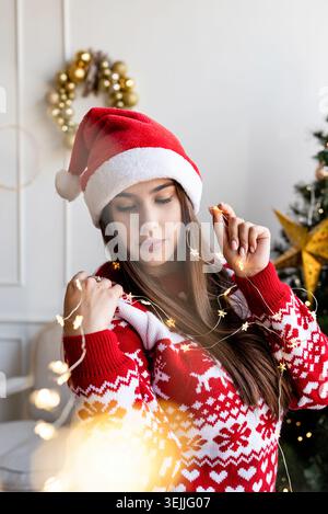 Giovane donna con cappello e maglione di babbo natale che regge splendide luci di natale Foto Stock