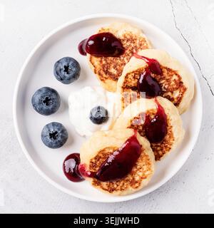 Vista dall'alto delle frittelle di formaggio con panna acida, marmellata di mirtilli e mirtilli Foto Stock