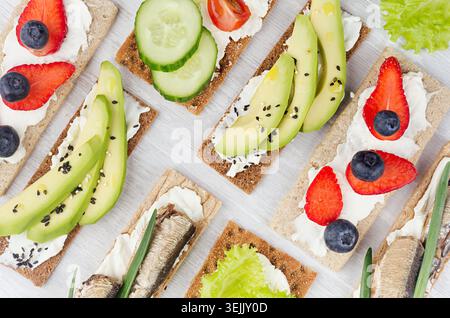Panini aperti leggeri e dolci estivi su pane patatine con verdure, frutta matura, conserve di pesce, formaggio spalmabile su un composto morbido e leggero Foto Stock