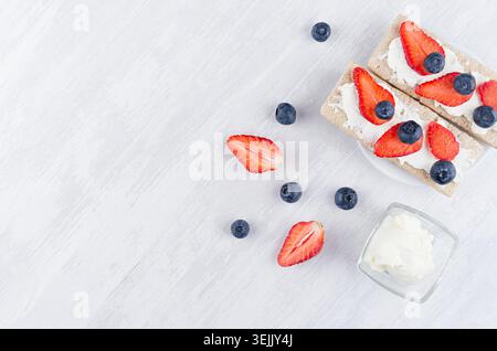Frutta fresca estiva sano antipasto di pane croccante di segale integrale con fette di fragola mature, mirtillo, formaggio cremoso dolce Foto Stock
