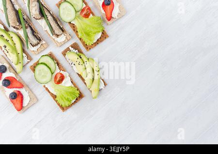 Panini aperti leggeri e dolci estivi su pane patatine con verdure, frutta matura, conserve di pesce, formaggio spalmabile su un composto morbido e leggero Foto Stock