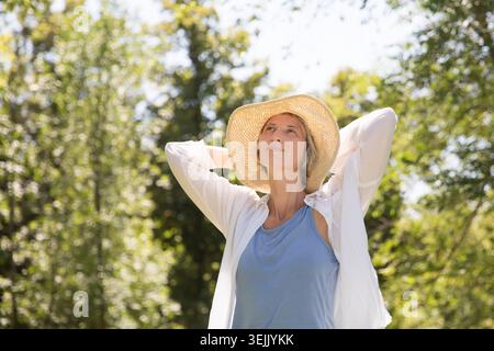 Donna sorridente di mezza età che indossa un cappello estivo in giardino Foto Stock