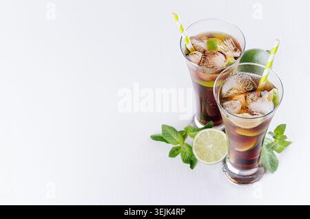 Cocktail al rum e alla cola in bicchieri con bollicine, cubetti di ghiaccio, lime, menta a foglia su morbido sfondo bianco chiaro con spazio per copiare, t Foto Stock