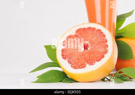Primo piano a fette di pompelmo rotonde con succo rosa e foglie verdi su un tavolo di legno bianco, spazio per copiare, macro. Foto Stock