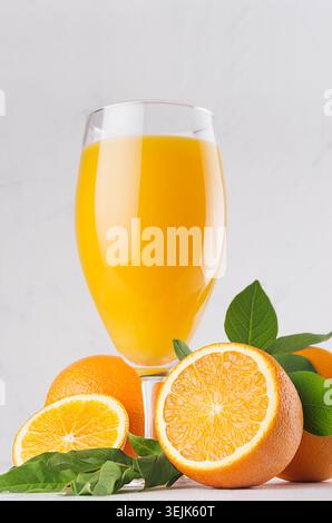 Succo d'arancia fresco con fette di arance e foglie verdi giovani primo piano su un morbido sfondo in gesso chiaro, verticale. Foto Stock