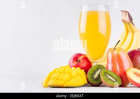 Succo esotico d'arancia di frutta diversa - mango, kiwi, banana, pera, pesca - con ingredienti su sfondo di legno bianco, closeu Foto Stock