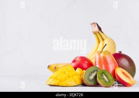 Mix di frutta colorata - frutta intera e succose fette a fette - mango, banana, pera, pesca, kiwi, nactarina su soffice ba di legno bianco Foto Stock