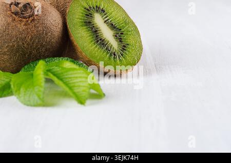 Kiwi verde maturo e carnoso con una fetta succosa, foglie giovani su un morbido tavolo bianco chiaro, primo piano, vista dall'alto. Fondo di frutta tropicale. Foto Stock