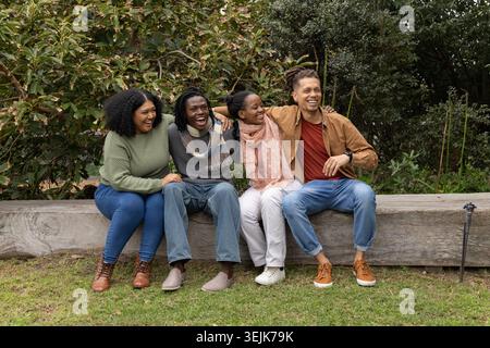 Amici diversi seduti da vicino su una panchina di legno nel giardino del parco, con sciarpe e sorrisi. Quartetto, all'aperto, naturale, informale, stock, natura, greene Foto Stock