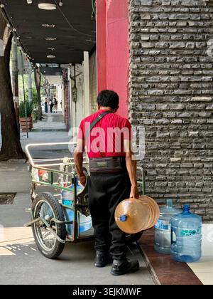 Un addetto alla consegna dell'acqua gestisce grandi caraffe d'acqua in bottiglia su un marciapiede a città del Messico, riflettendo la dipendenza urbana dall'acqua potabile privata Foto Stock