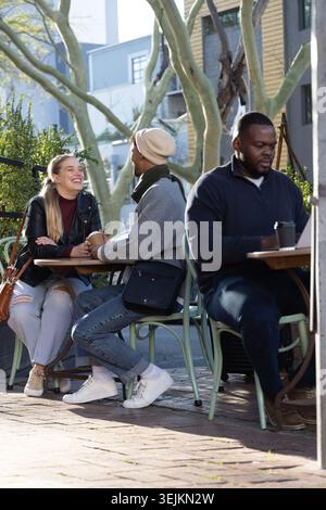 Coppia che ride e si piega, tenendosi per mano nel patio della caffetteria sul lato della strada con un computer portatile nelle vicinanze. Esterno, terrazza, marciapiede, Unione, conversazione, gioia, Foto Stock