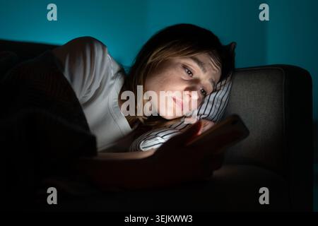 Donna che utilizza il telefono cellulare mentre si trova a letto di notte, che soffre di insonnia post-disgregazione. Ansia. Foto Stock