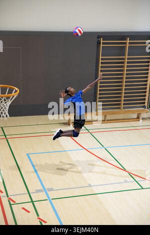 Giovanissimo afroamericano che salta con una maglia blu-rossa-bianca-blu sul campo da palestra. Atletica, aviotrasportata, palla, cerchio Foto Stock