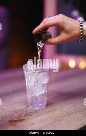 Barman che versa liquido dal jigger alla tazza di plastica con ghiaccio Foto Stock
