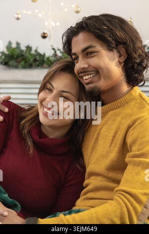 Coppia seduta sul divano, appoggiata insieme, con la parte superiore marrone e la maglia della senape, garland dietro. Partner, salotto, accogliente, caldo Foto Stock