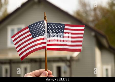 Due bandiere americane in mano che sventolano di fronte alla casa suburbana. Foto Stock