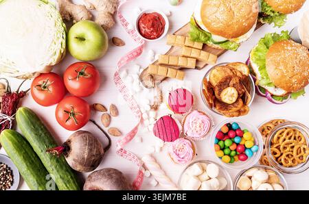 Concetto di cibo sano e malsano. Frutta e verdura, dolci e fast food su sfondo bianco in legno con un metro a nastro. Vista dall'alto, disposizione piatta Foto Stock